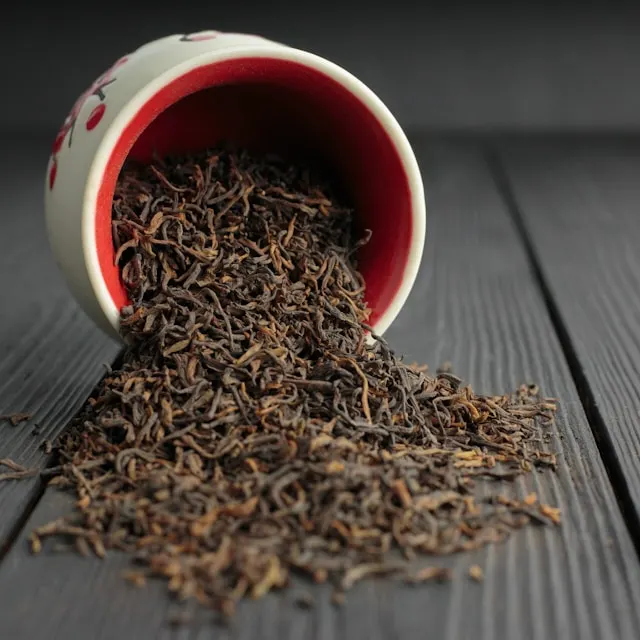 A bowl of dried-up black tea leaves spilling from the bowl onto the counter. The focus is emphasized on the leaves.