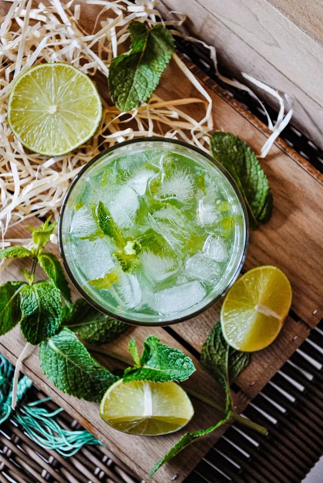 A large glass bowl full of cut up limes and little mint leaves. The bowl is on top of a wooden cutting board with other ingredients for the Green Tea Gimlet Cocktail.