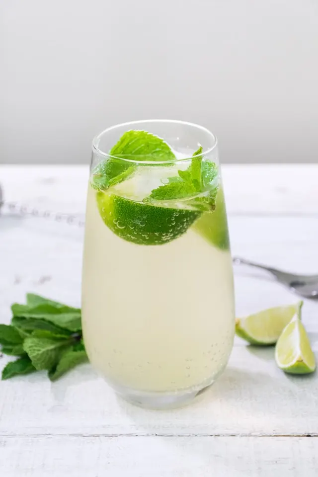 A glass of green tea gimlet cocktail with gin, slices of lime, and mint leaves.