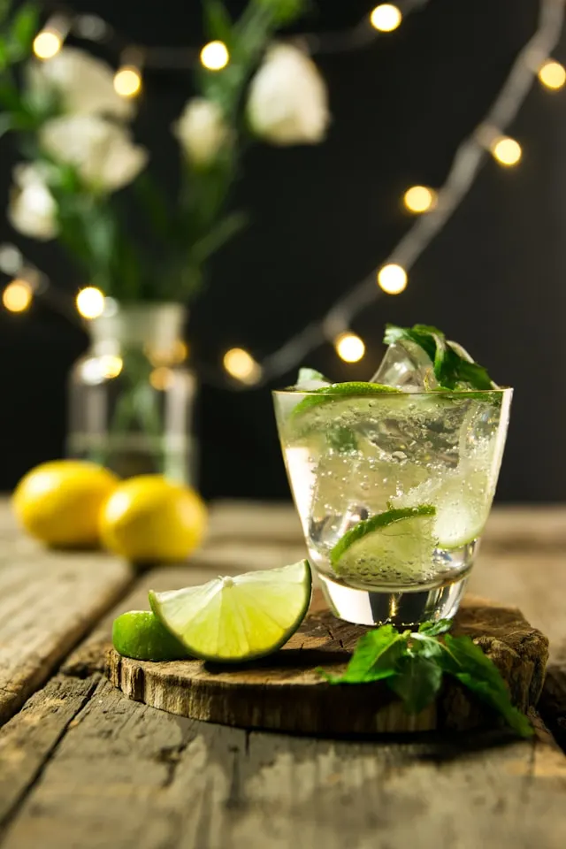 Green tea gimlet cocktail with slices of fresh green lime and cubes of ice inside a shot glass.