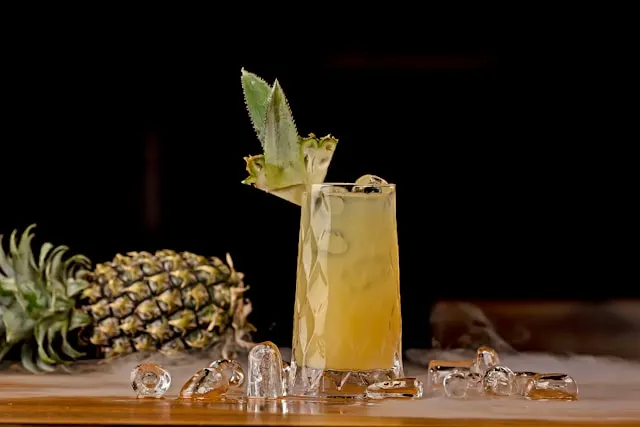 Green tea martini with pineapple and lime juice and a slice of pineapple on glass rim.