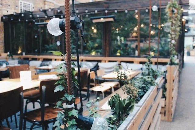 Varietea of Alcohol’s outdoor patio that is fenced-in with wooden tables inside and aesthetic light bulbs hanging overtop. 