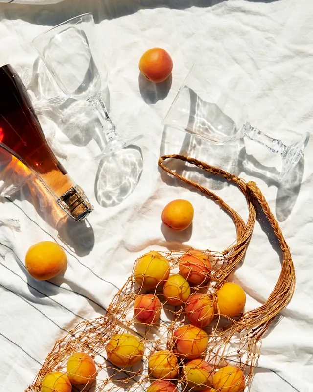 Photo shows a ginger ale bottle with empty glass cups and a bag full of ripe peaches.