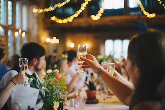 Multiple people sitting at a long rectangular table and raising their glasses to cheers in the Varietea of Alcohol’s Event Space. 