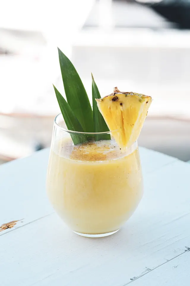 A glass of a green tea martini with pineapple and a chuck of fresh pineapple on the glass rim.