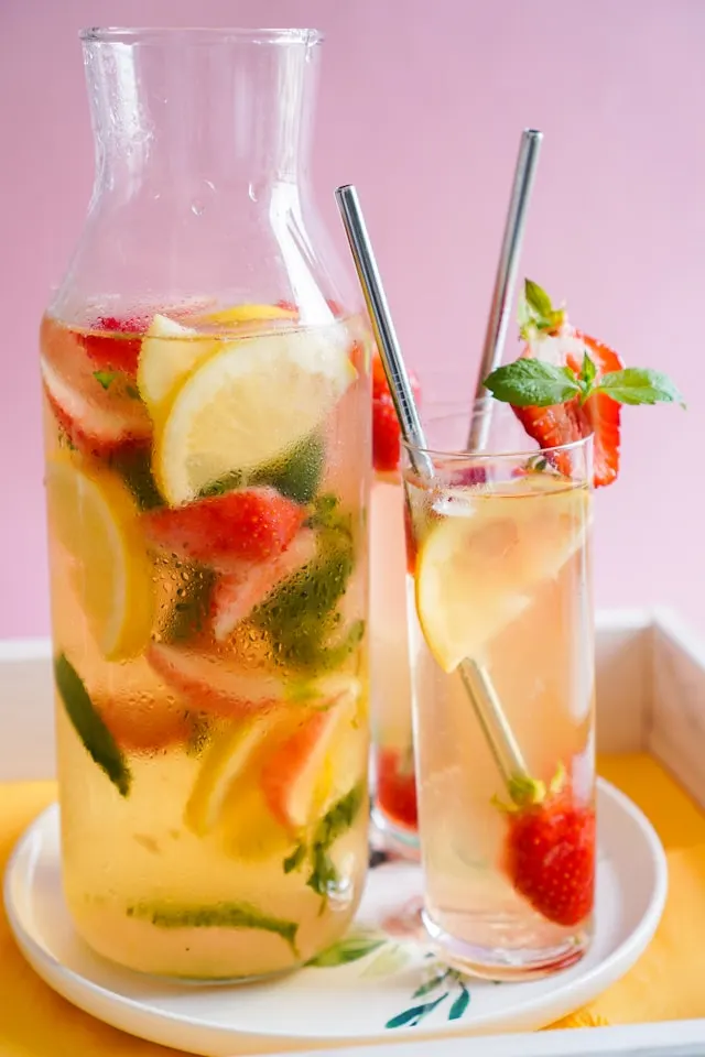 A glass teapot and a tall glass cup filled with slices of strawberries, lemons, and basil to make the cocktail taste sweet with the gin and black tea mixture.