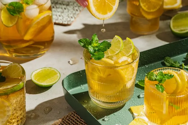 Multiple shot glasses with lemonade mixed with black tea and vodka. As well as slices of lemon and mint leaves in the drinks.