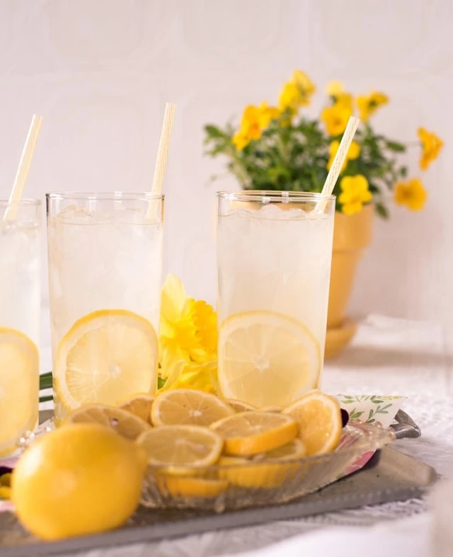 Three tall glasses filled with lemonade that is mixed with sweet black tea and vodka. As well as a slice of lemon in each glass cup. There are also slices of lemons on a plate beside the glasses.