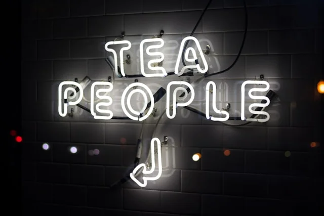 A white neon sign that says, ‘tea people’ and the light up sign is attached to a white wall.