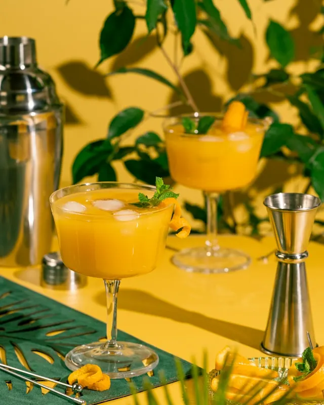 Two tall drinking glasses with cocktails, mint leaves and ice.